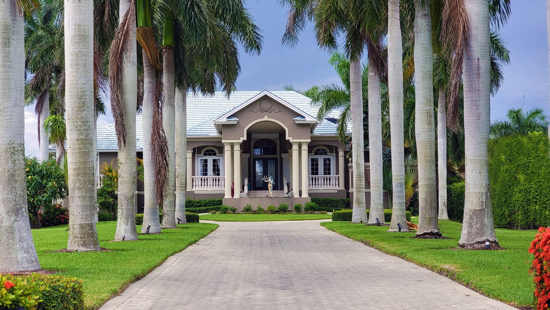 A beautiful residential house with palm trees lining the driveway under a clear sky