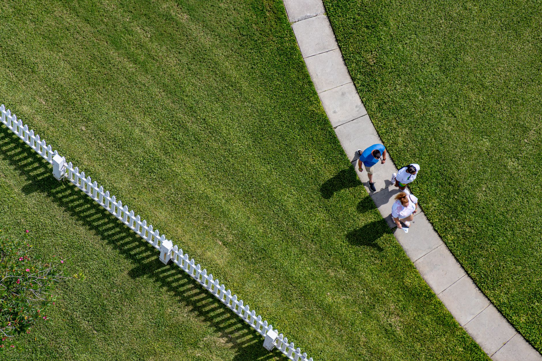 Aerial view of a curved sidewalk lined with healthy green lawn and a white fence in a Florida neighborhood